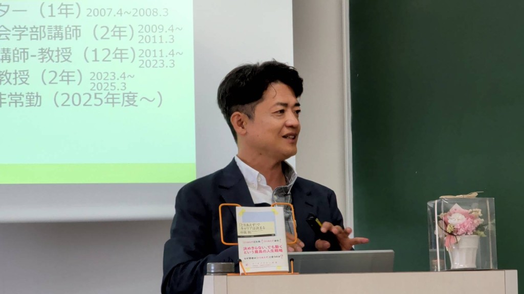 演台の前に立ち、書籍を示しながら笑顔で話す中嶌剛