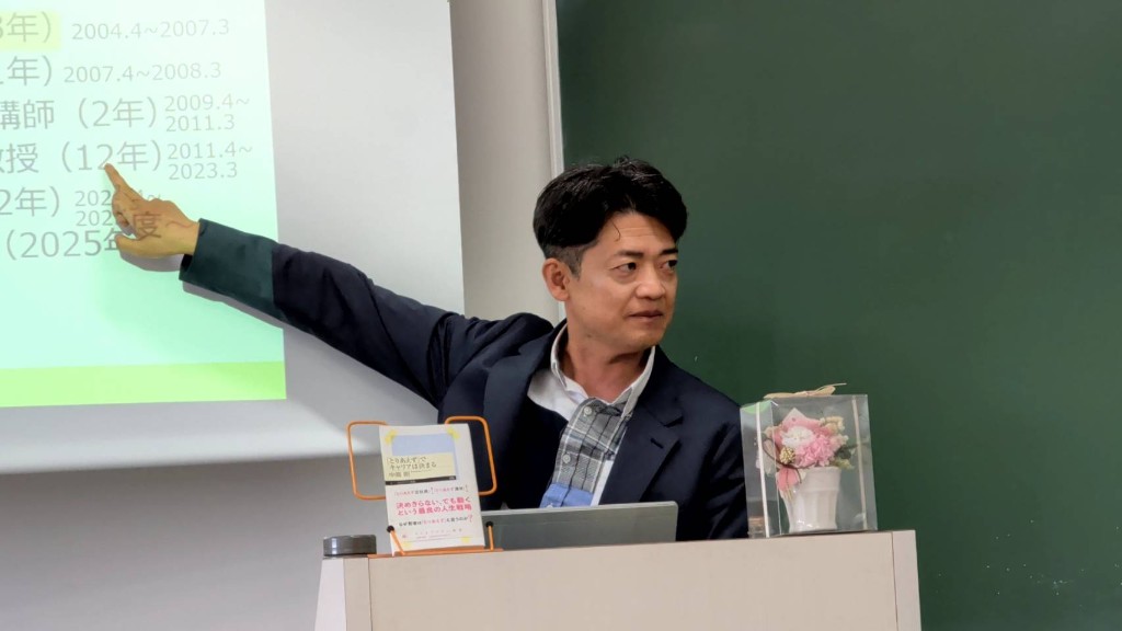 スクリーンに映した経歴を指しながら講演する中嶌剛