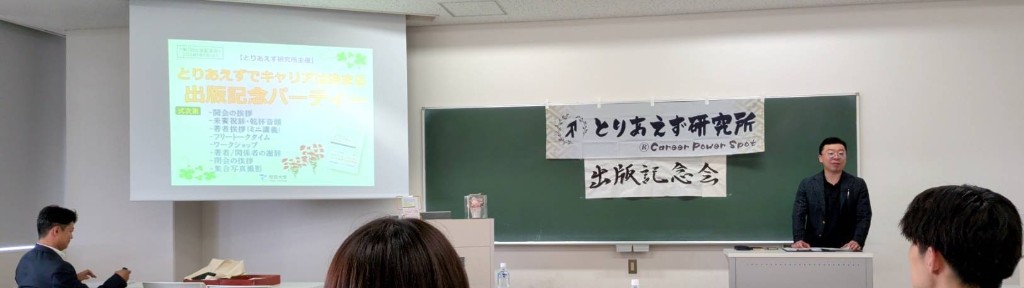 式次第を映したスクリーンと「出版記念会」の横断幕がある会場