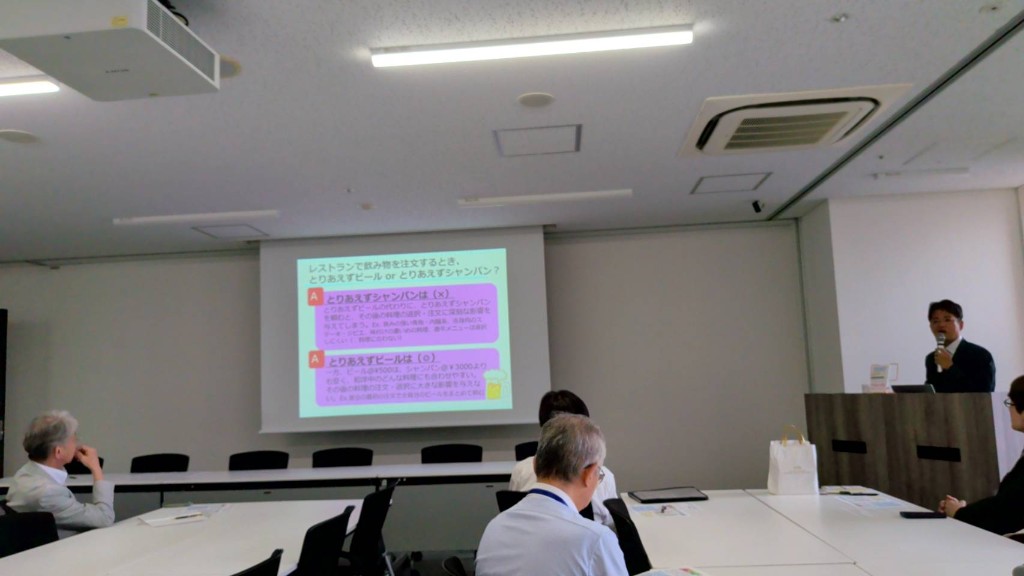 スクリーンに日常生活の活用例を映し、参加者が聴く会場